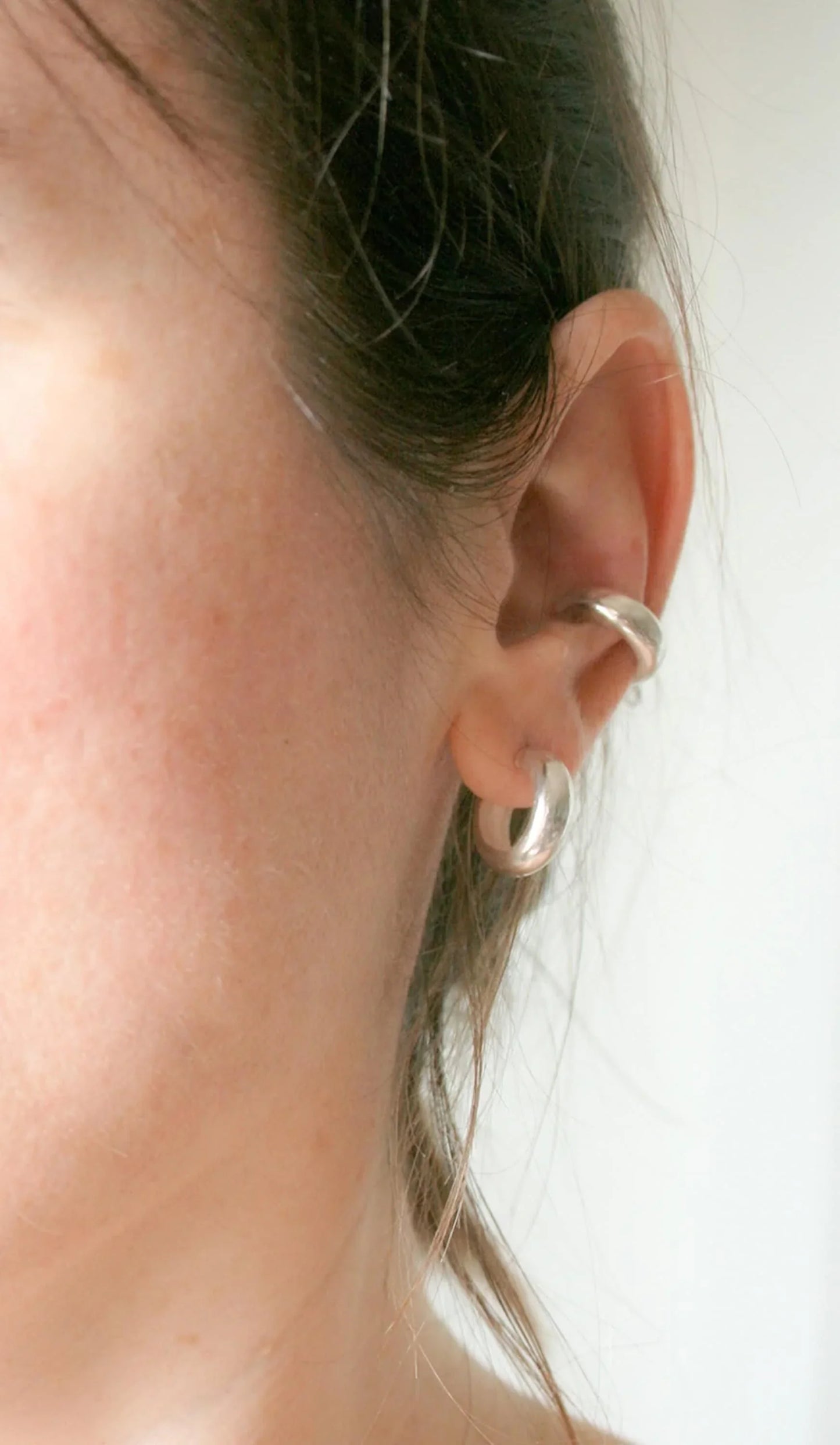 Close-up of ear with two minimalist silver hoop earrings, cartilage and lobe piercing jewelry
