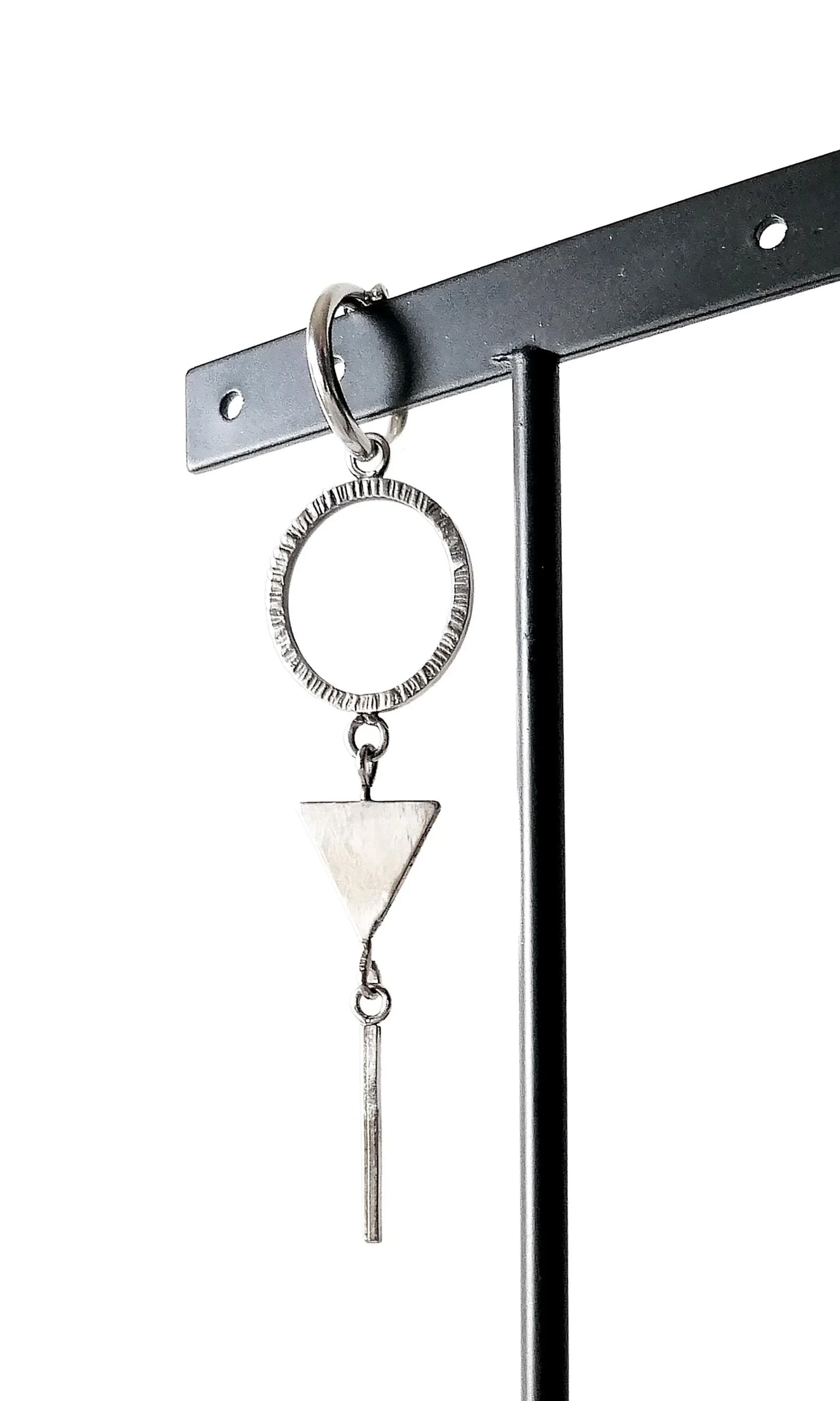 Geometric silver dangle earring with circle, triangle, and bar shapes on display stand