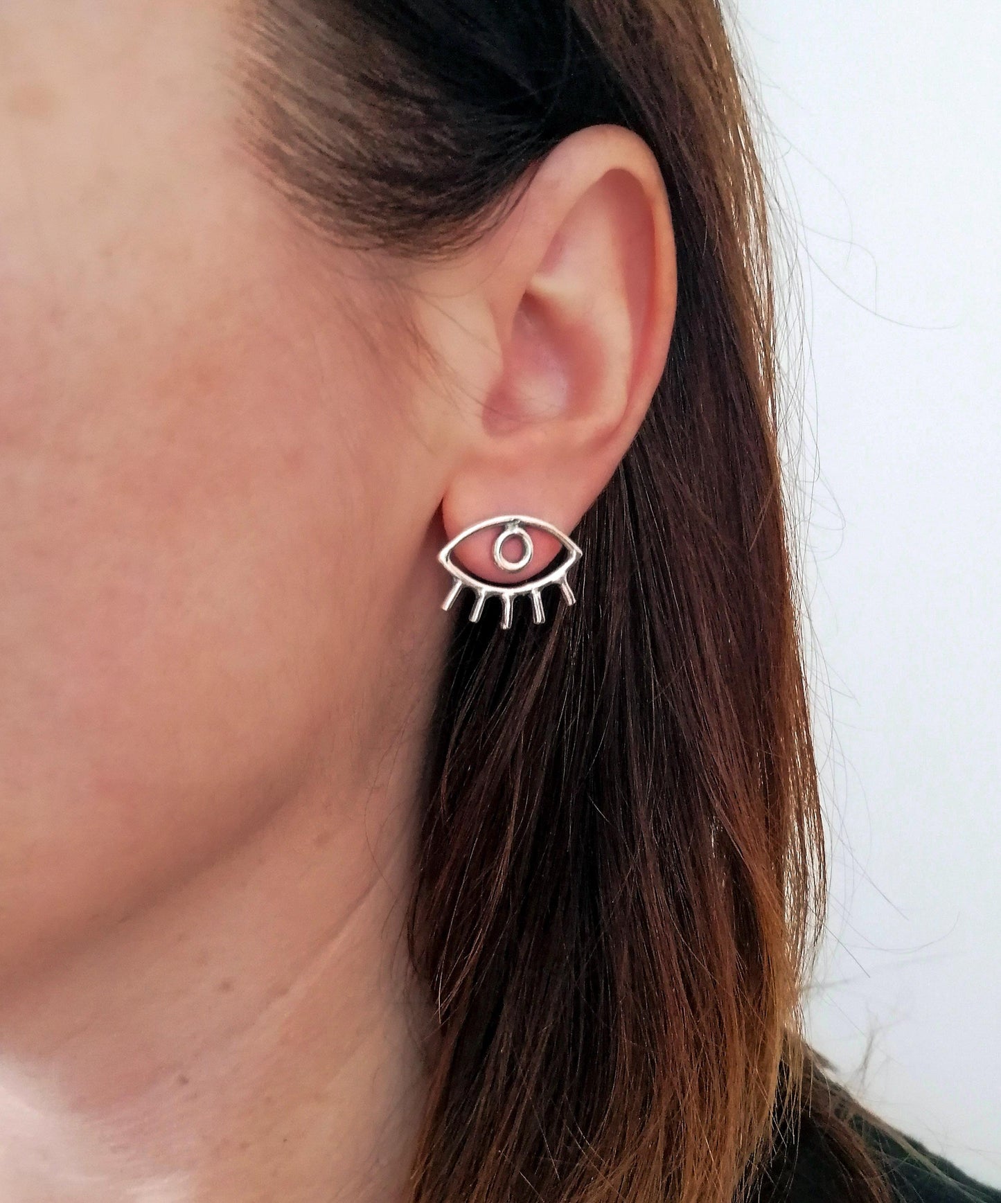 Silver eye-shaped stud earring with lashes on woman's ear, minimalist jewelry