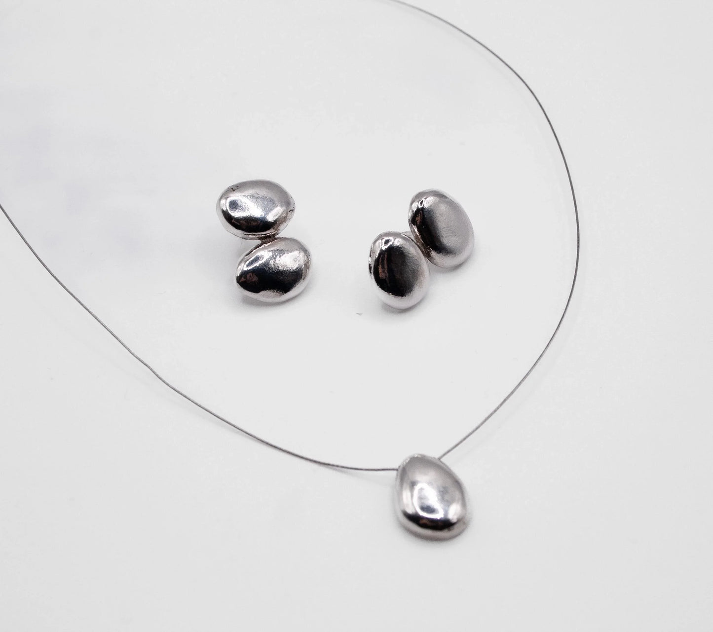 Minimalist silver pebble pendant necklace and four loose pebble charms on white background