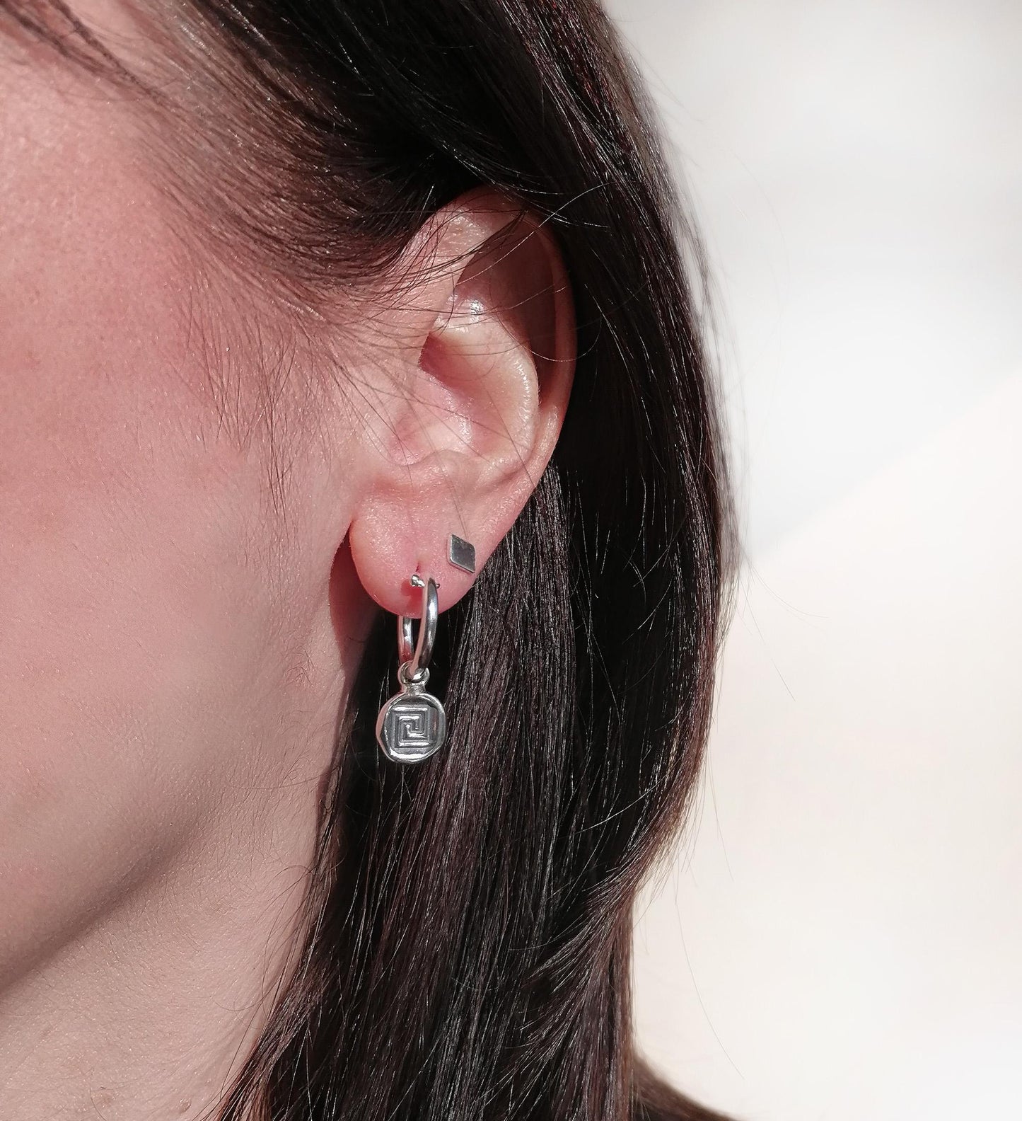 Woman wearing geometric silver hoop and stud earrings, close-up ear jewelry