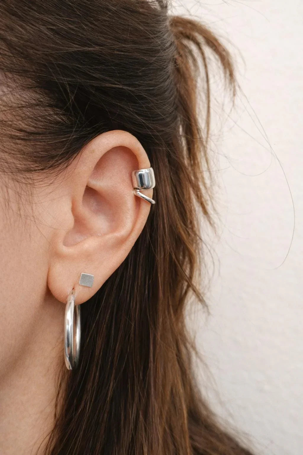 Woman wearing silver ear cuff and geometric hoop and square stud earrings