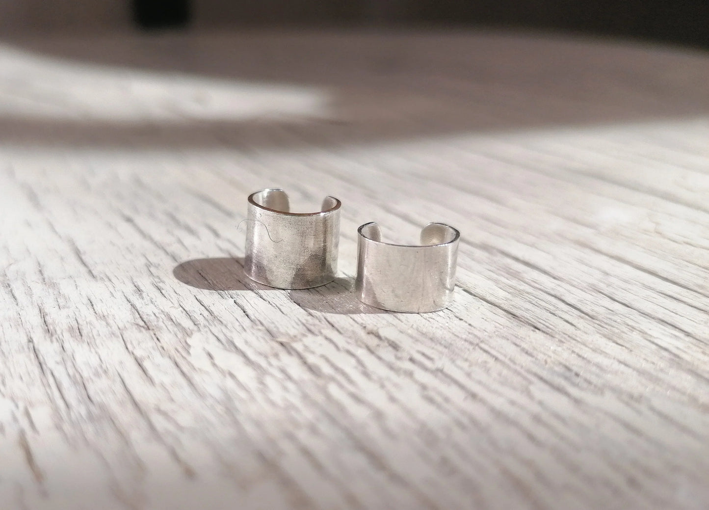 pair of minimalist silver ear cuffs on light wood surface
