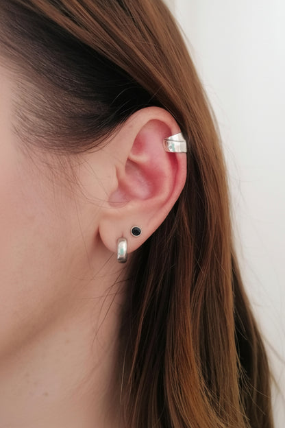 Close-up of an ear with silver earrings against a neutral background