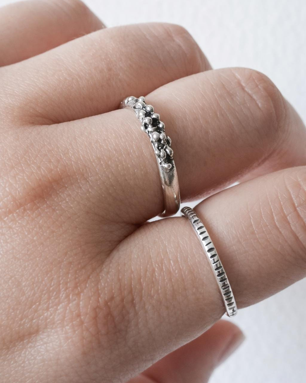 Close-up of a hand wearing two silver rings on a white background