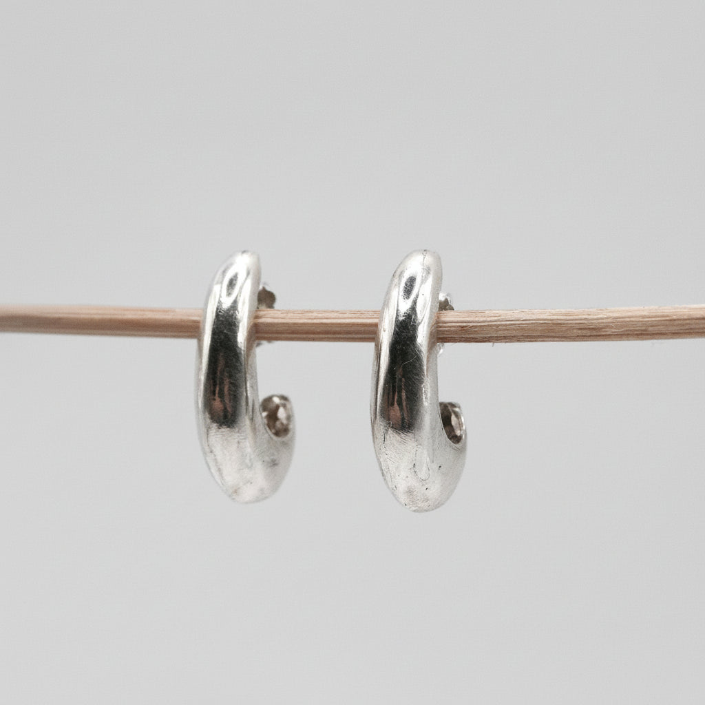 Silver hoop earrings on a thin rod against a light gray background