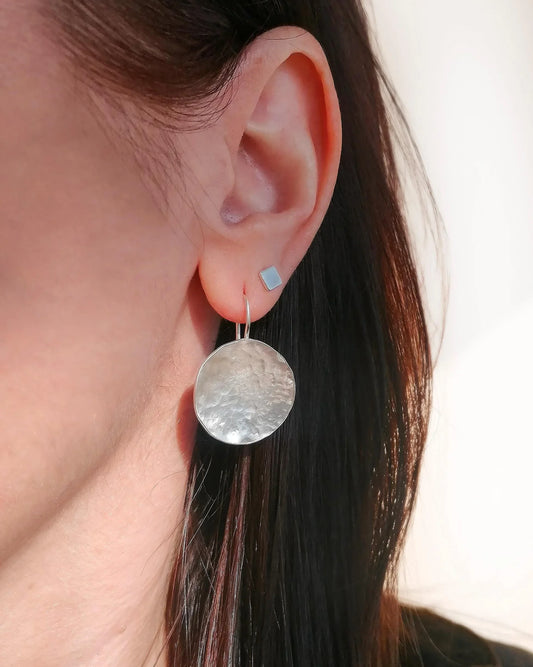 Close-up of an ear wearing a silver earring with a blurred background