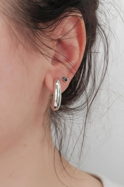 Close-up of an ear wearing a silver hoop earring with a plain background