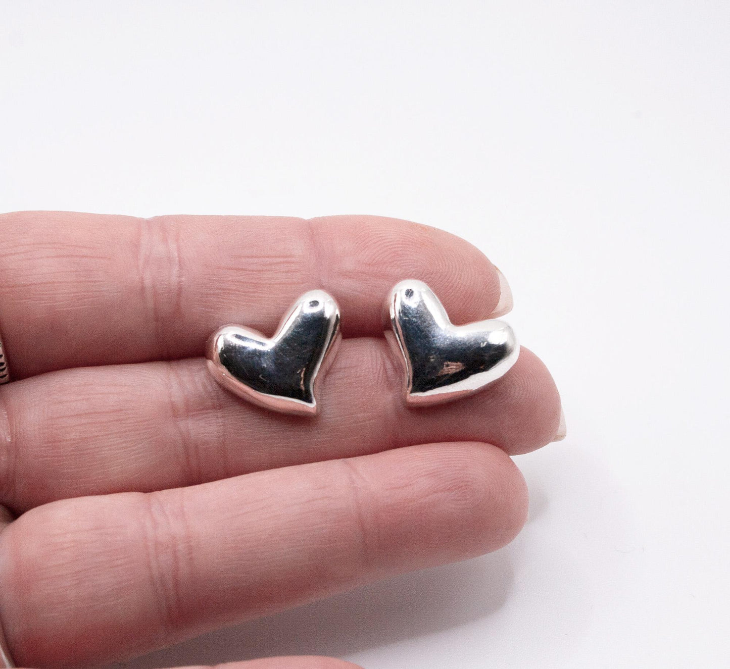 Pair of shiny silver heart stud earrings displayed on a hand, minimalist jewelry