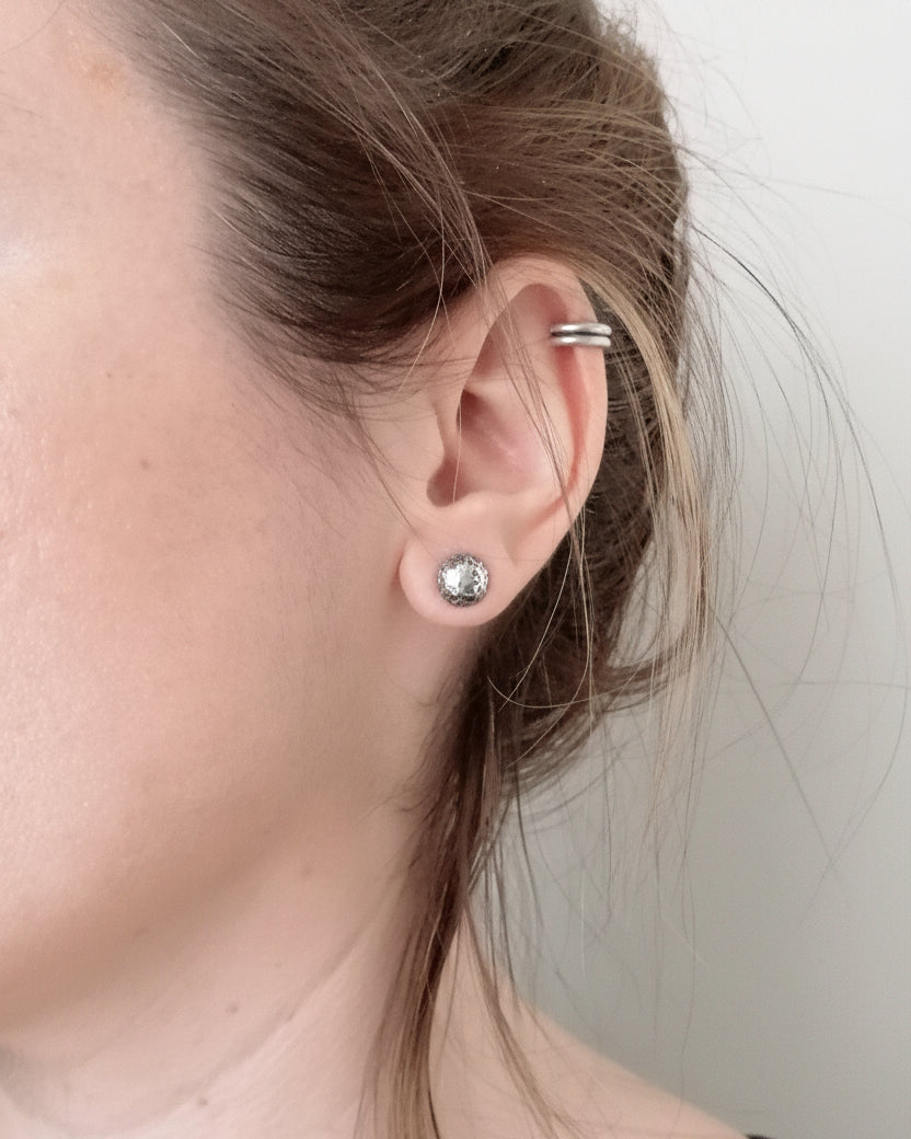 Close-up of an ear with a silver earring and hoop, against a neutral background.