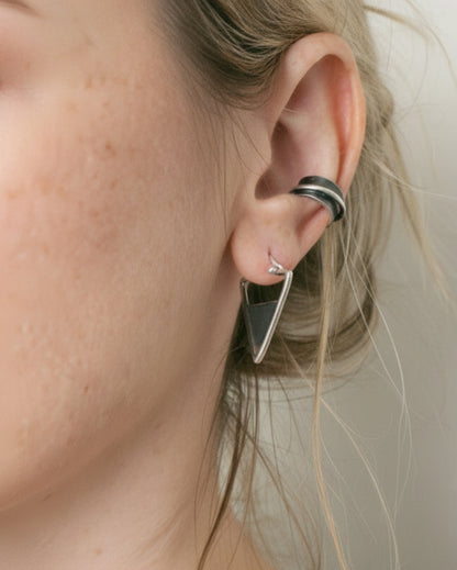 Close-up of a person wearing a silver triangle earring and hoop earrings.