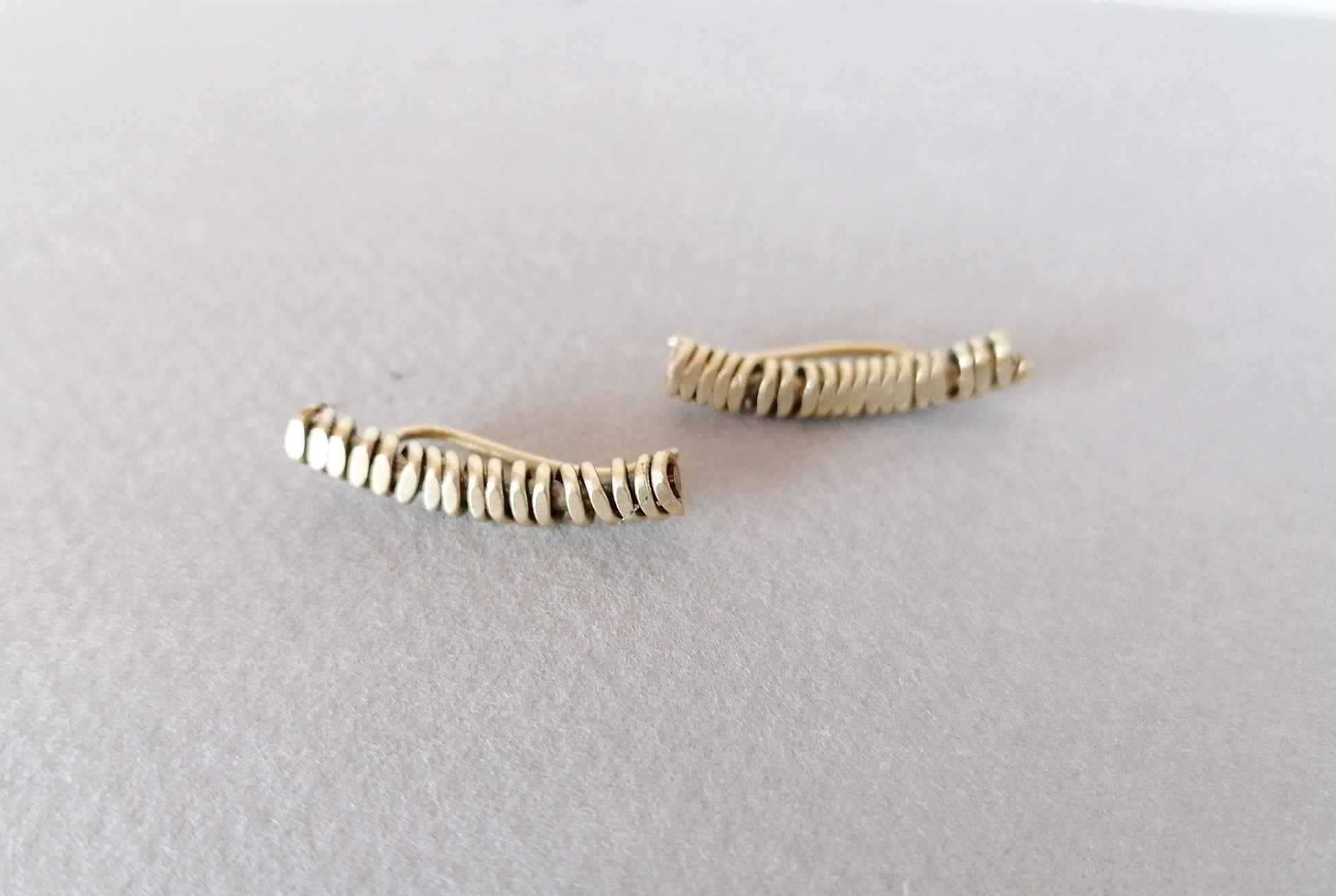 Two gold-colored ear cuffs on a light gray background