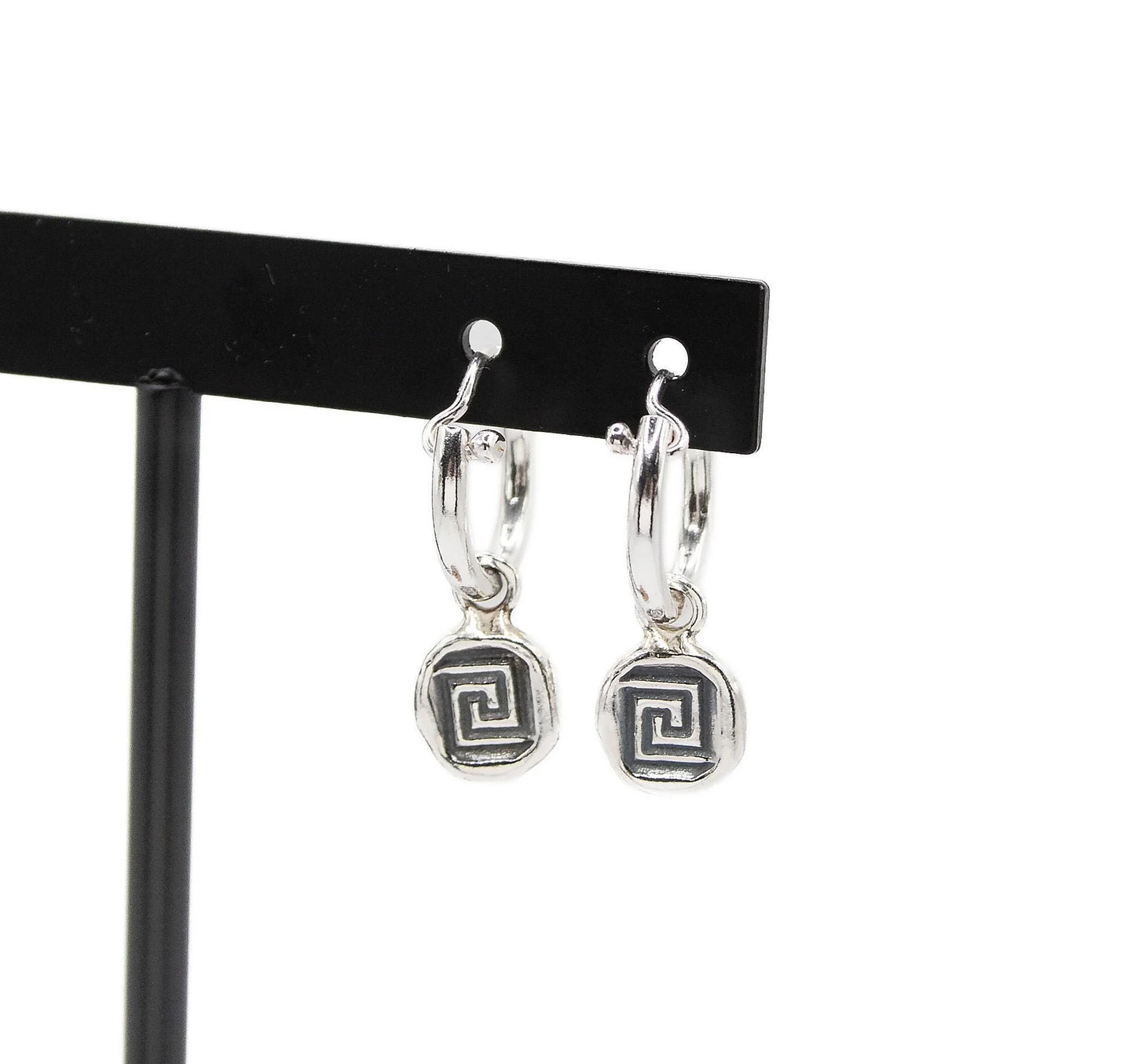 Silver hoop earrings with geometric spiral charms on a black display stand