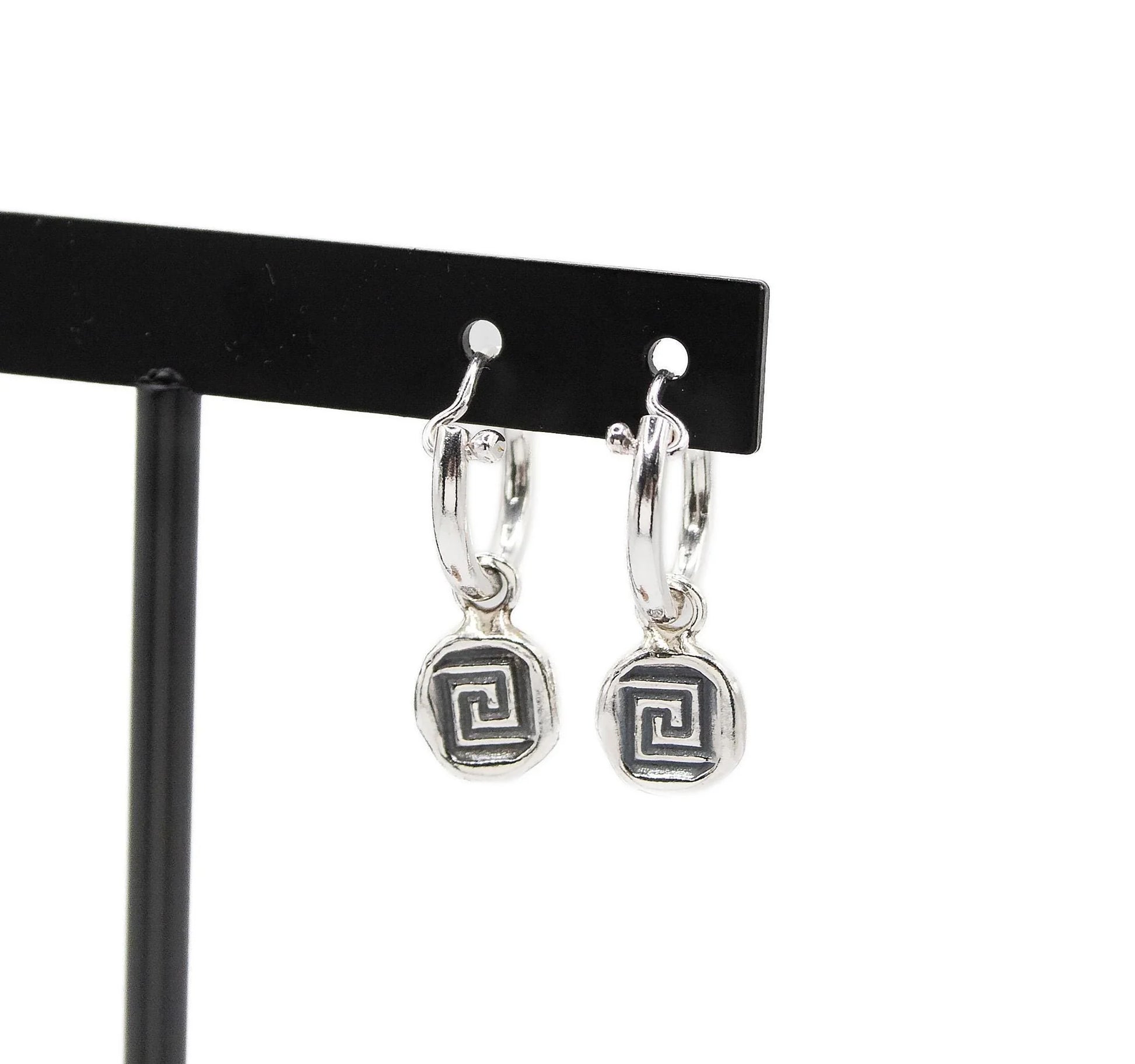 Silver hoop earrings with geometric spiral charms on a black display stand