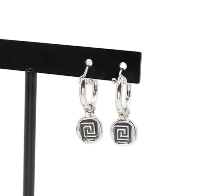 Silver hoop earrings with geometric spiral charms on a black display stand