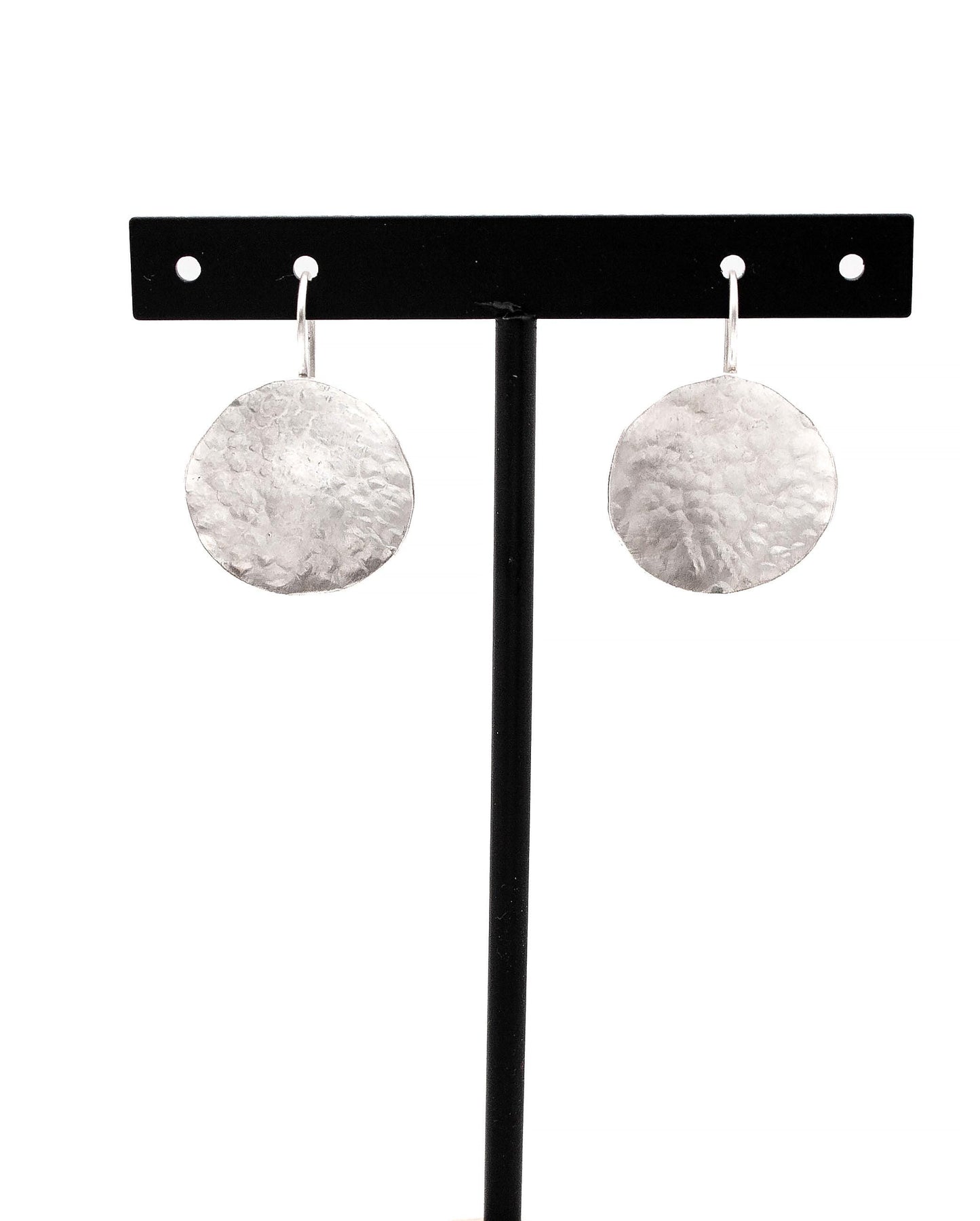 Hammered silver disc dangle earrings displayed on a black stand, minimalist jewelry