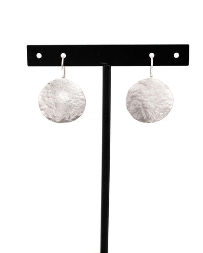 Hammered silver disc dangle earrings displayed on a black stand, minimalist jewelry