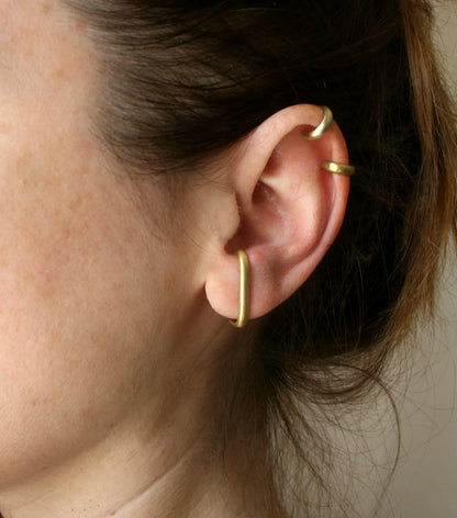 Ear with three minimalist gold ear cuffs jewelry, close-up on ear lobe and cartilage