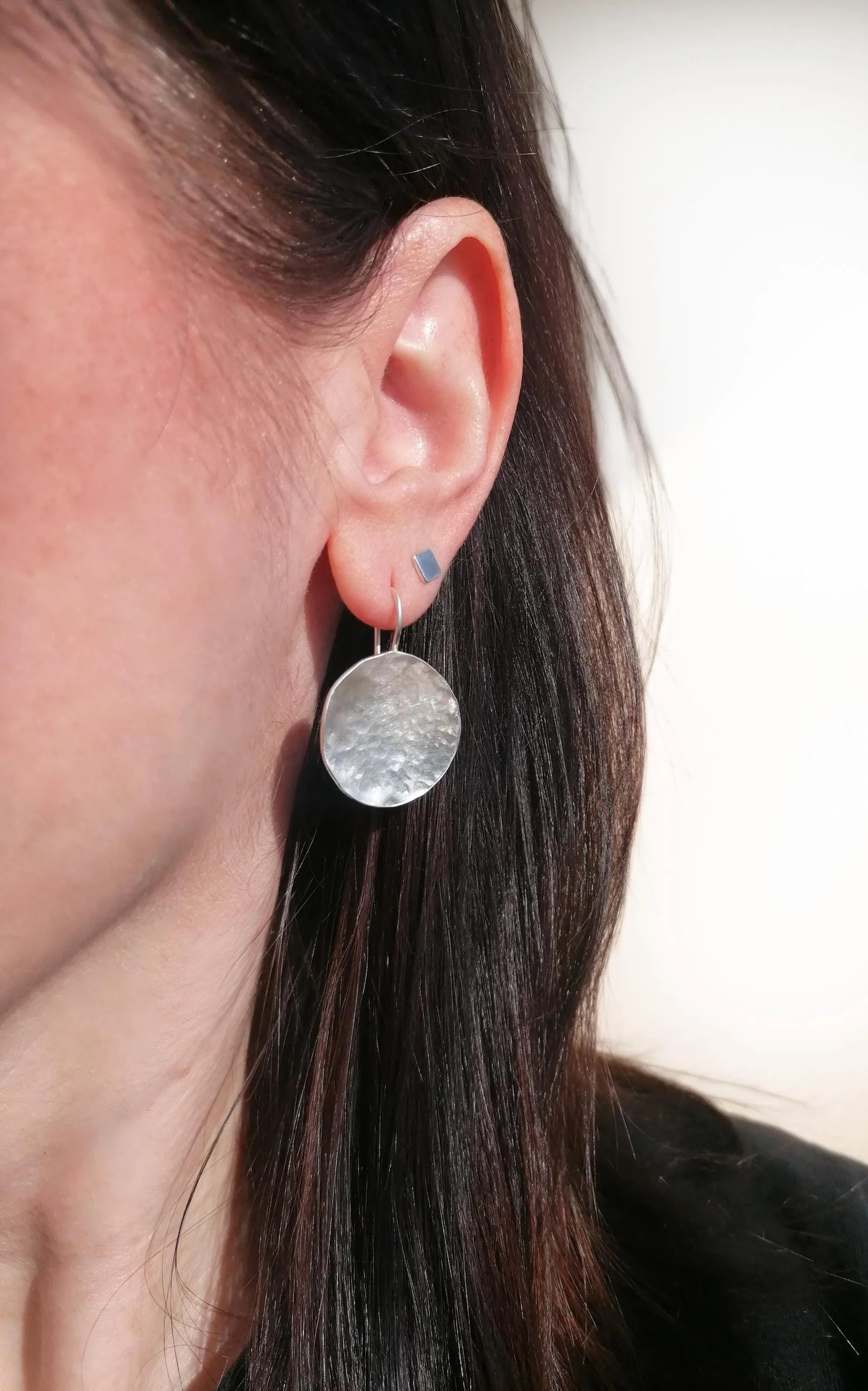 Woman wearing a hammered silver disc dangle earring and small geometric stud