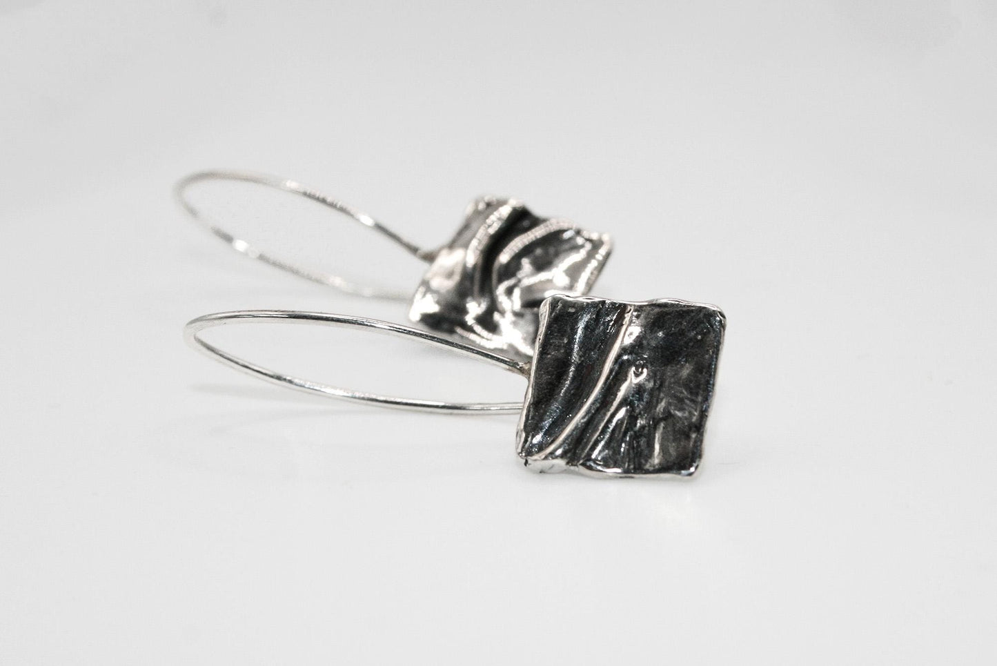 Handcrafted silver drop earrings with abstract square design on white background