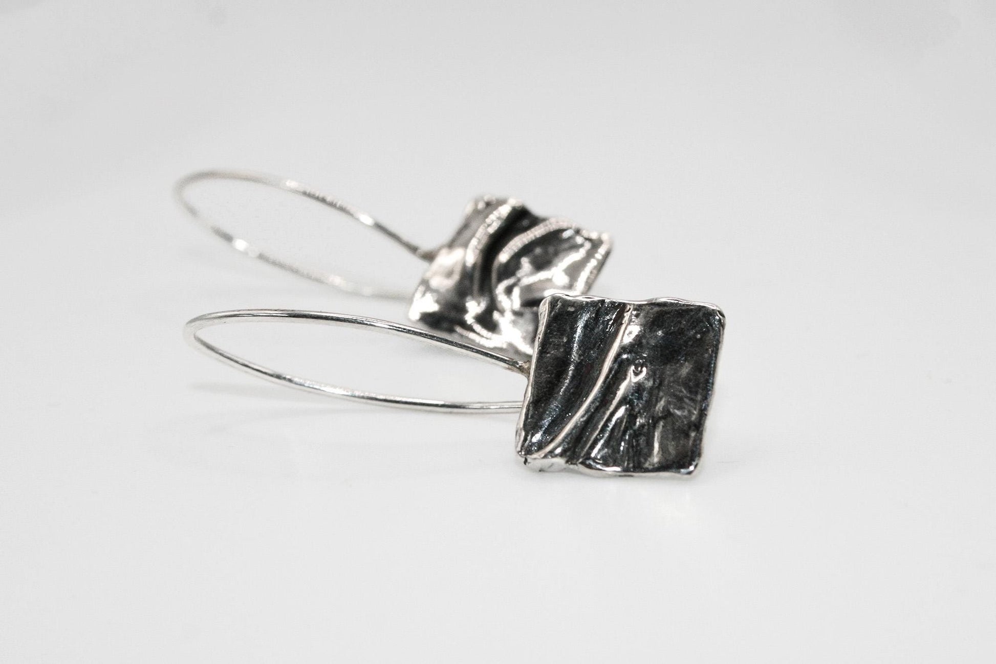 Handcrafted silver drop earrings with abstract square design on white background
