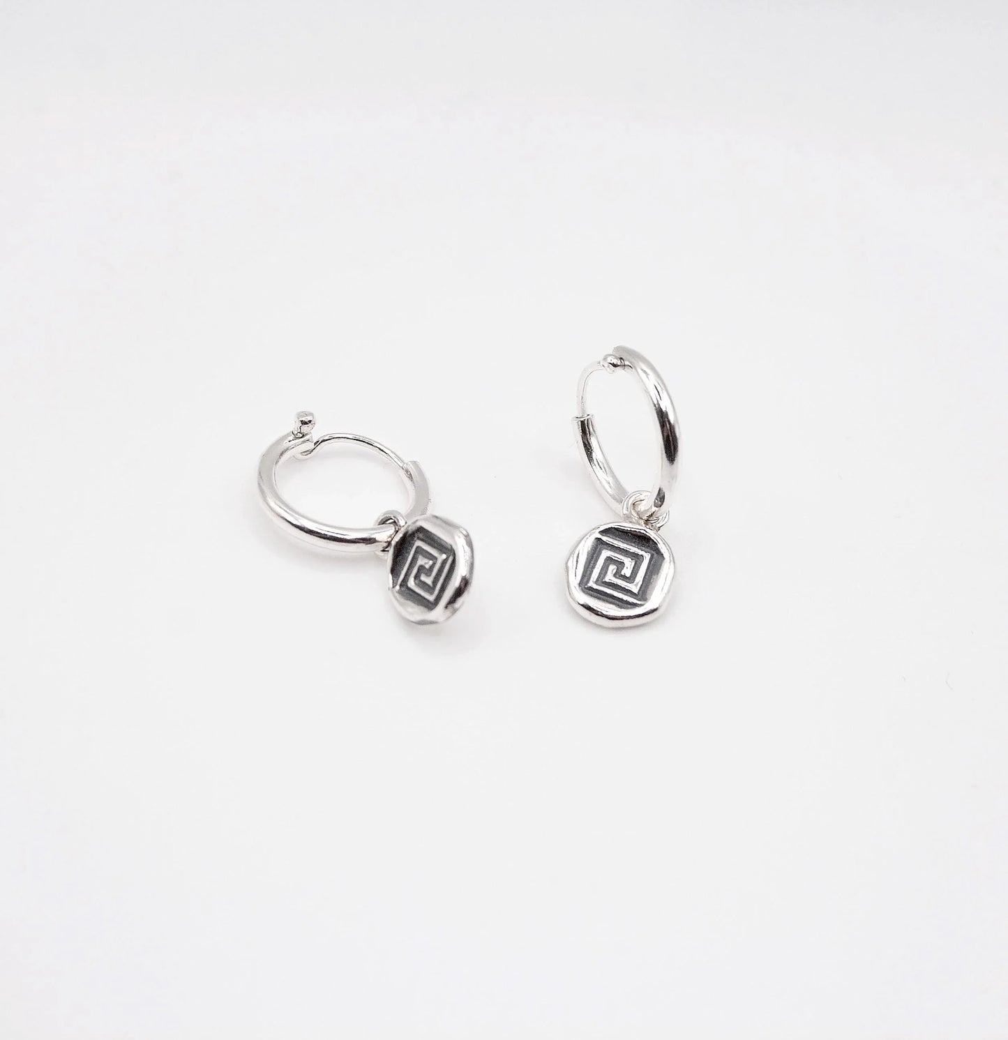 Sterling silver hoop earrings with geometric swirl charms on white background