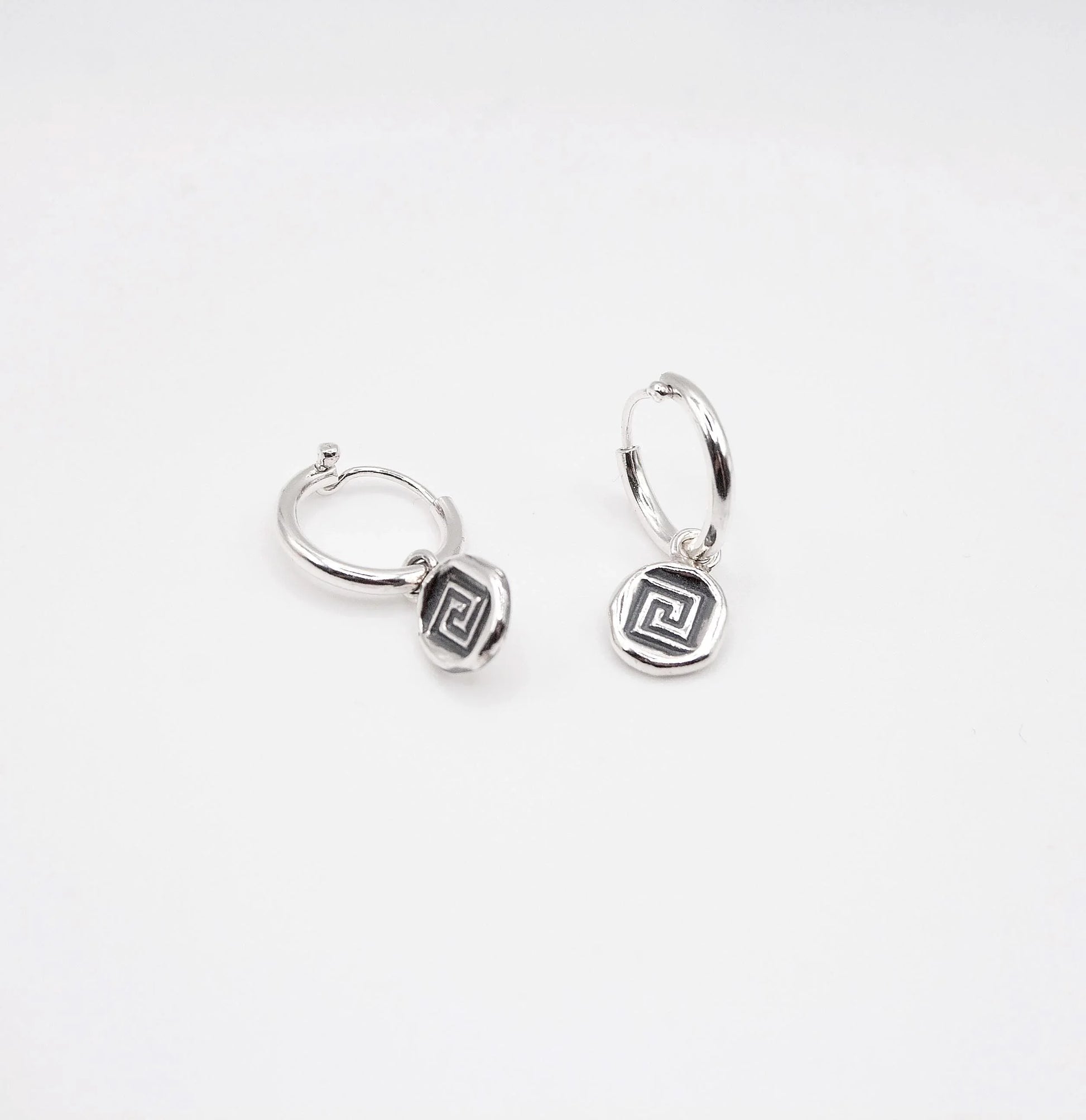 Sterling silver hoop earrings with geometric swirl charms on white background