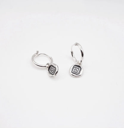 Sterling silver hoop earrings with geometric swirl charms on white background