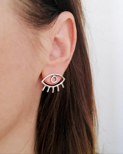 Silver eye-shaped earring worn by a person with long brown hair.