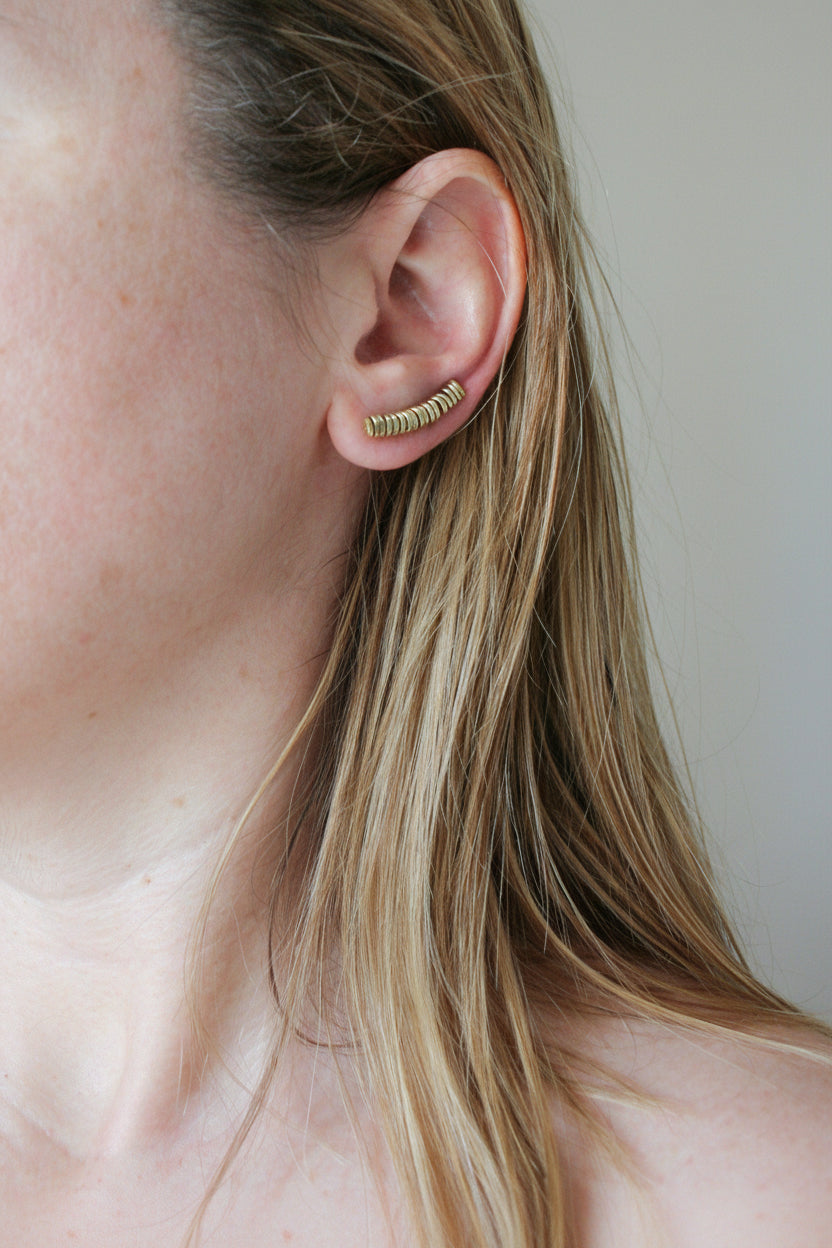 Close-up of a person wearing a gold earring with a neutral background