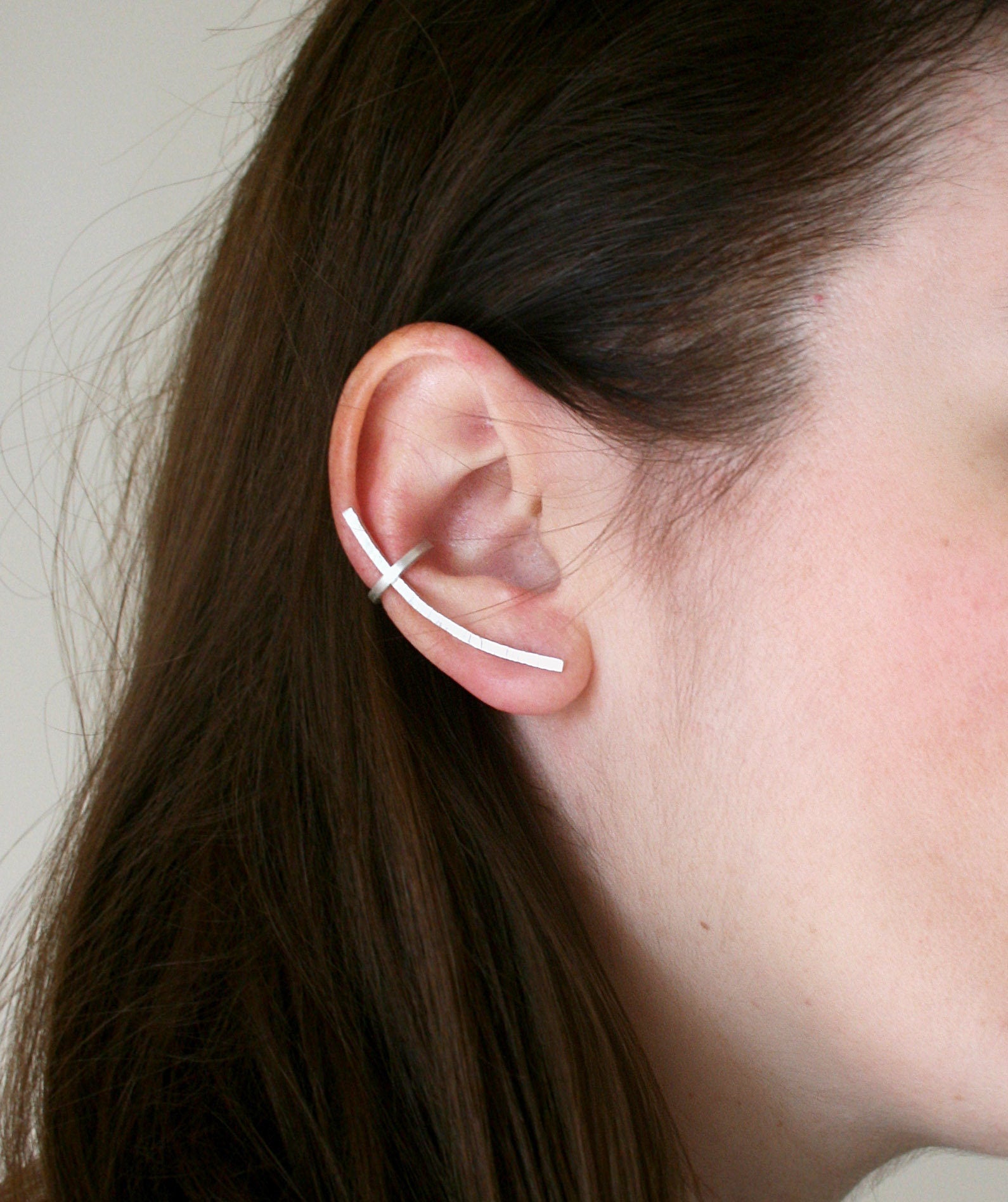 Close-up of an ear wearing a thin white earring against a neutral background
