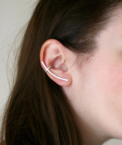 Close-up of an ear wearing a thin white earring against a neutral background