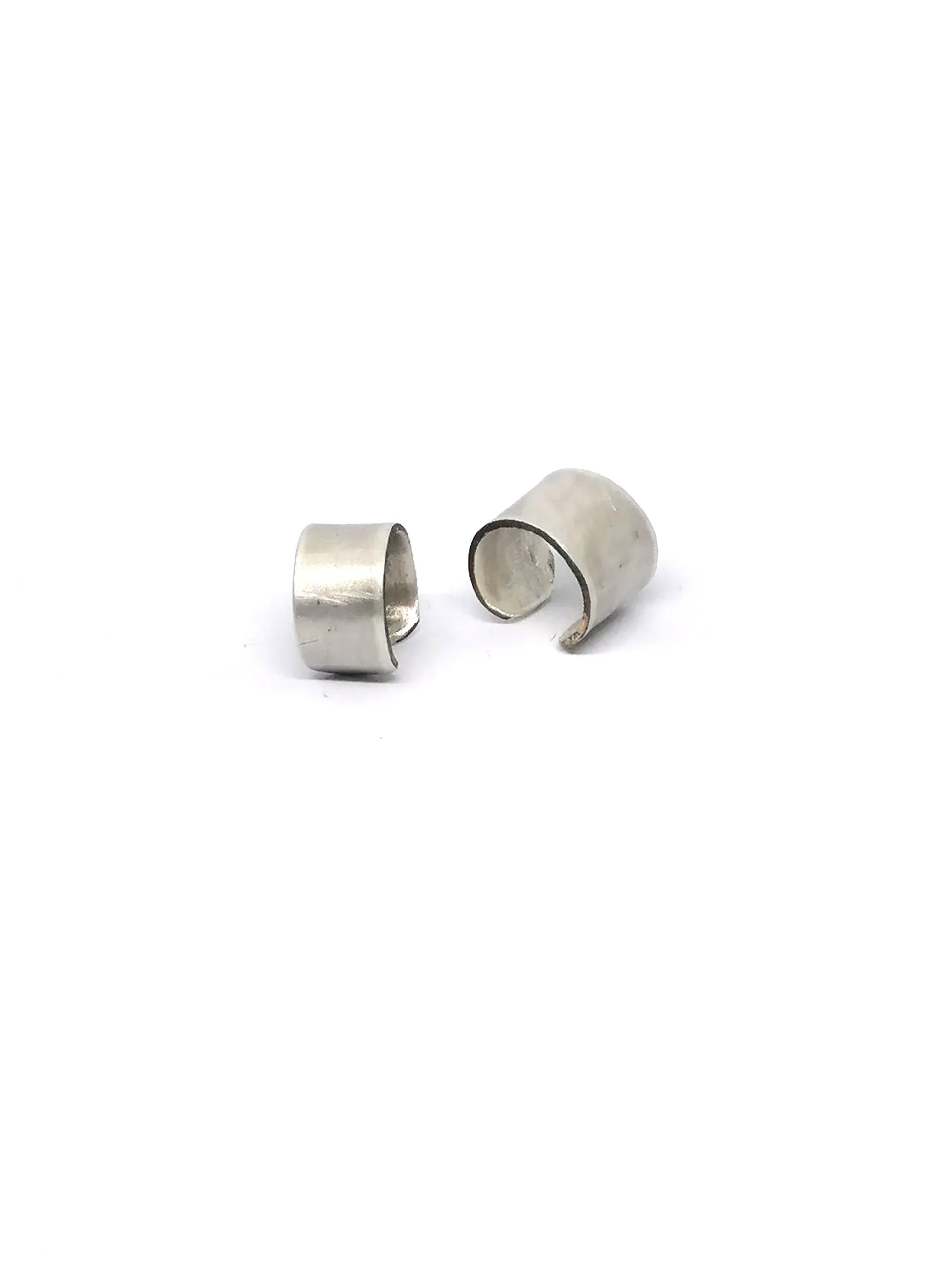 Pair of minimalist silver ear cuffs on white background, modern unisex jewelry