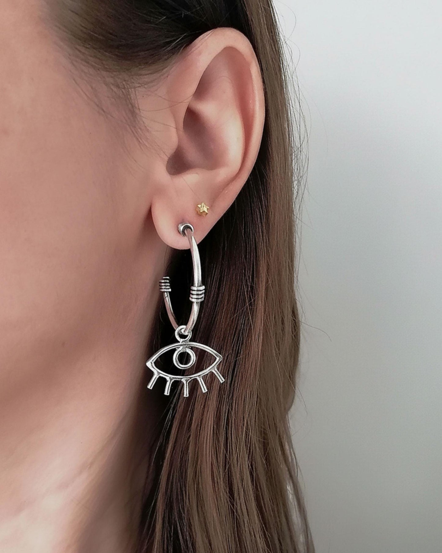 Close-up of an ear wearing a silver eye-shaped earring with a plain background