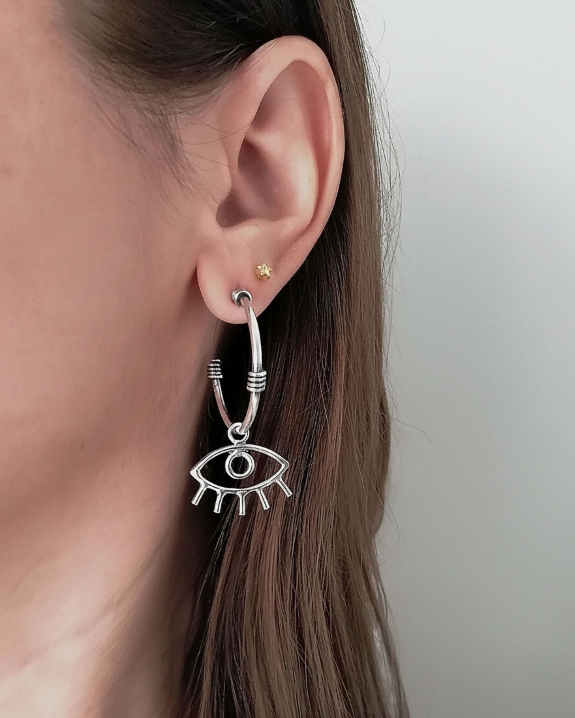 Close-up of an ear wearing a silver eye-shaped earring with a plain background