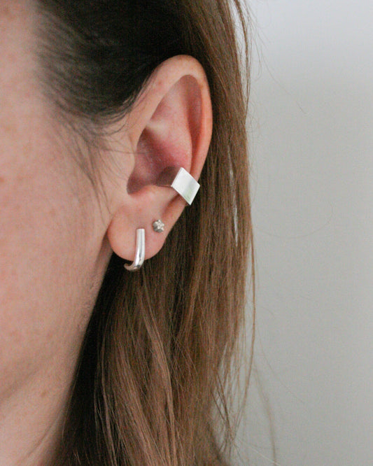 Close-up of an ear wearing a silver earring with a small gemstone on a plain background