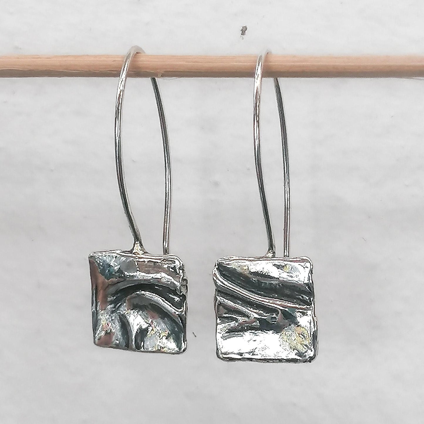 Abstract silver dangle earrings with textured square design on a minimalist background