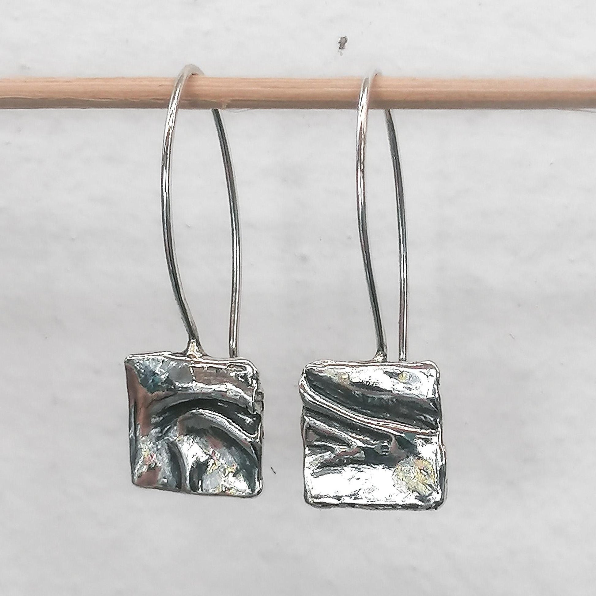 Abstract silver dangle earrings with textured square design on a minimalist background