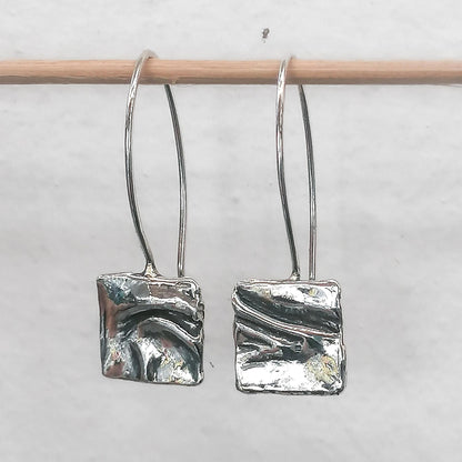 Abstract silver dangle earrings with textured square design on a minimalist background