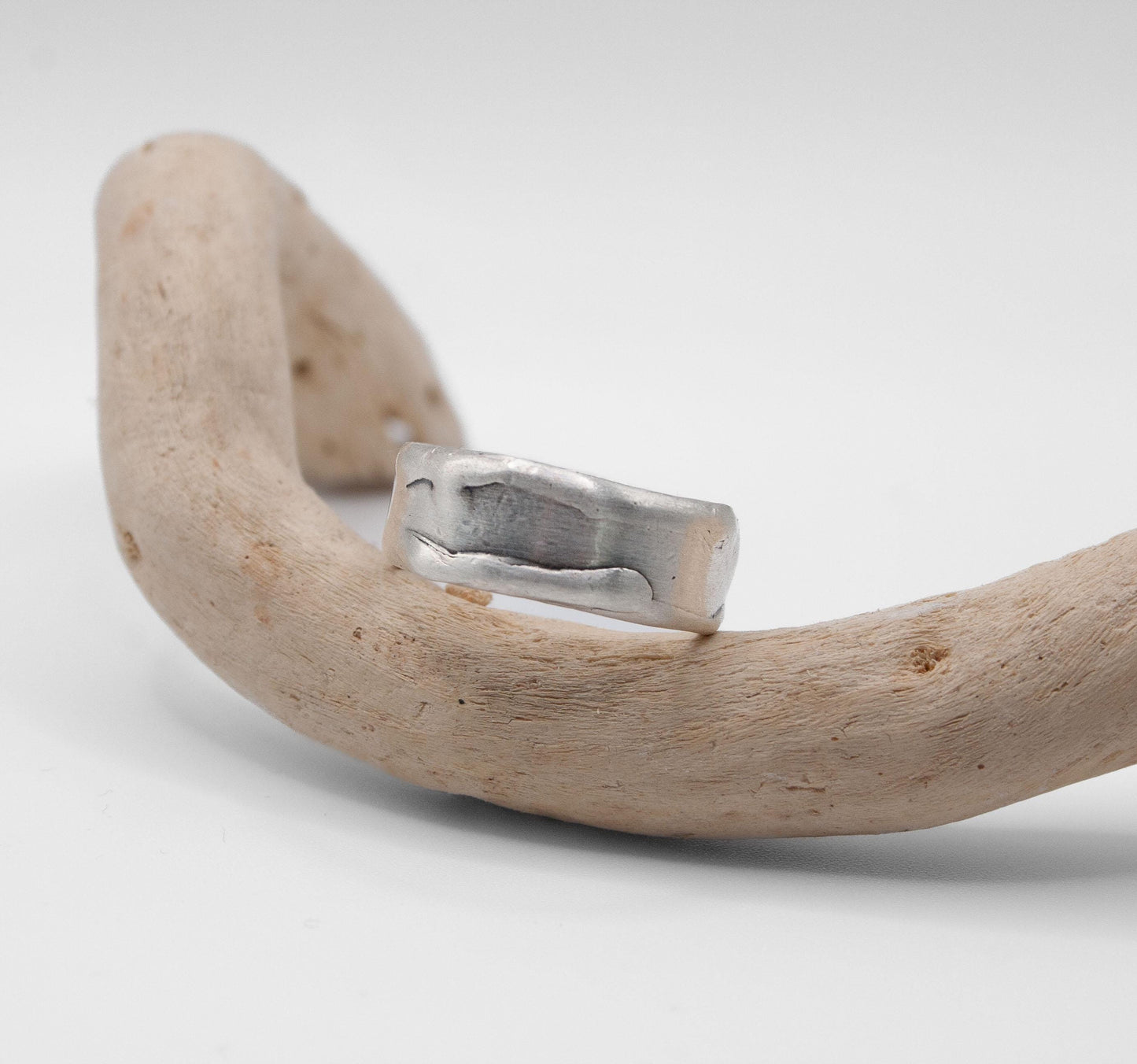 Silver ring on a curved piece of driftwood against a light gray background