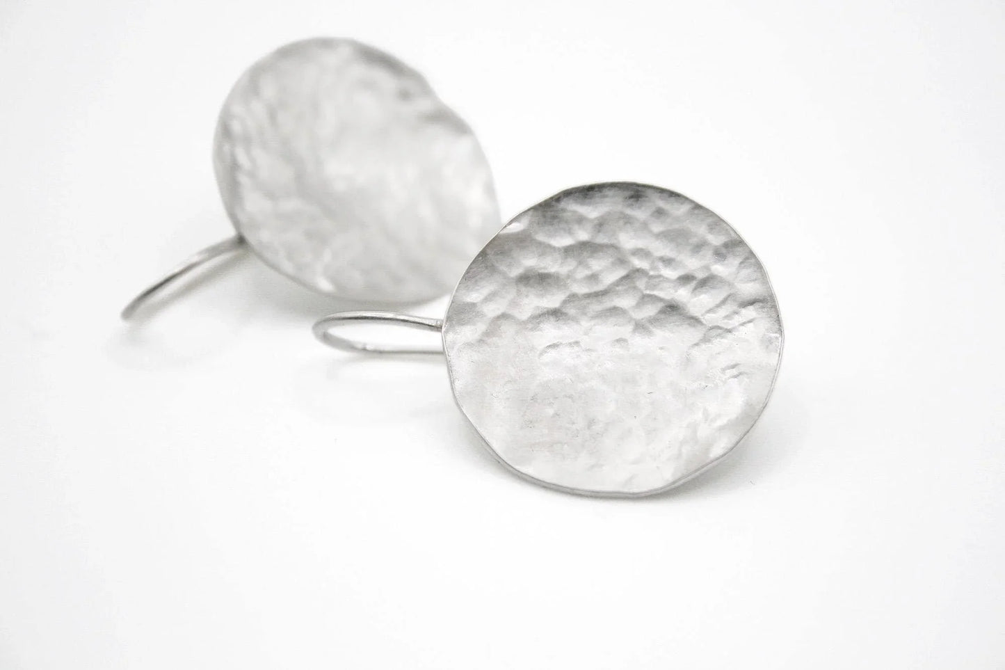 Hammered silver round dangle earrings with textured finish on white background