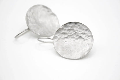 Hammered silver round dangle earrings with textured finish on white background
