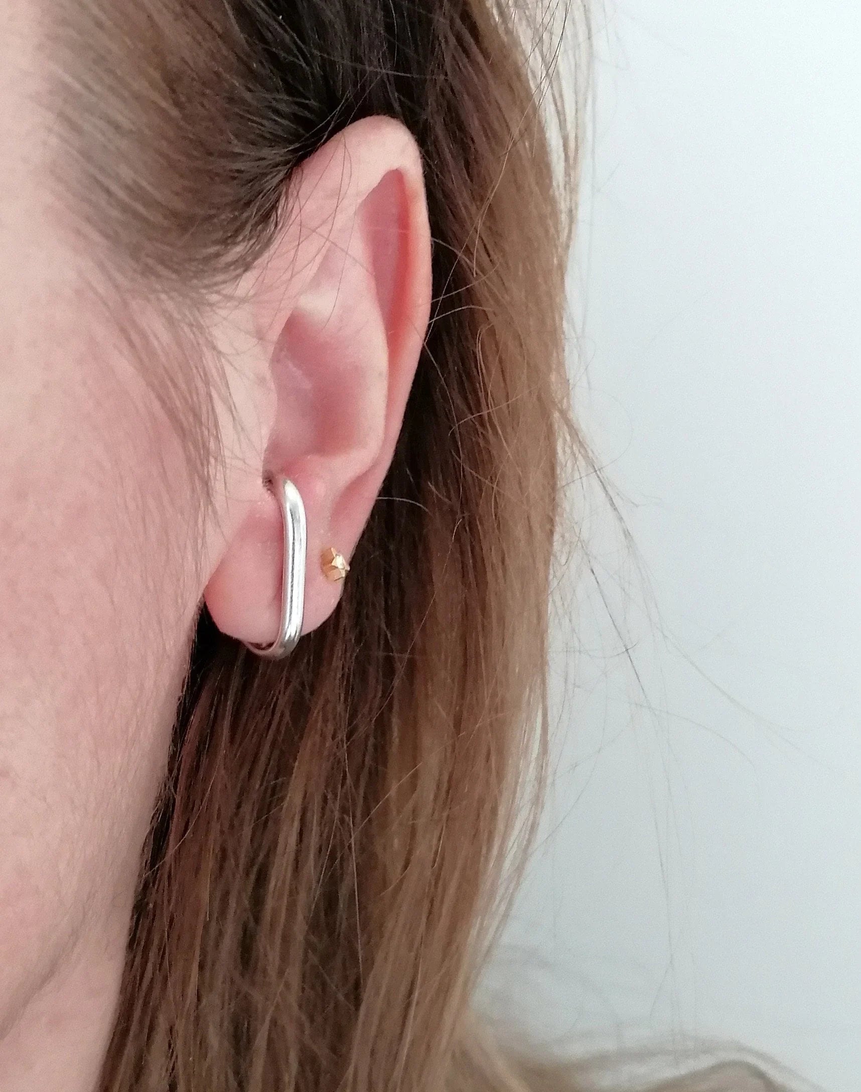 Woman wearing minimalist silver ear climber and small gold stud earring