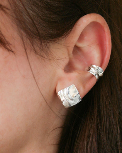 Silver earrings worn by a person with dark hair.