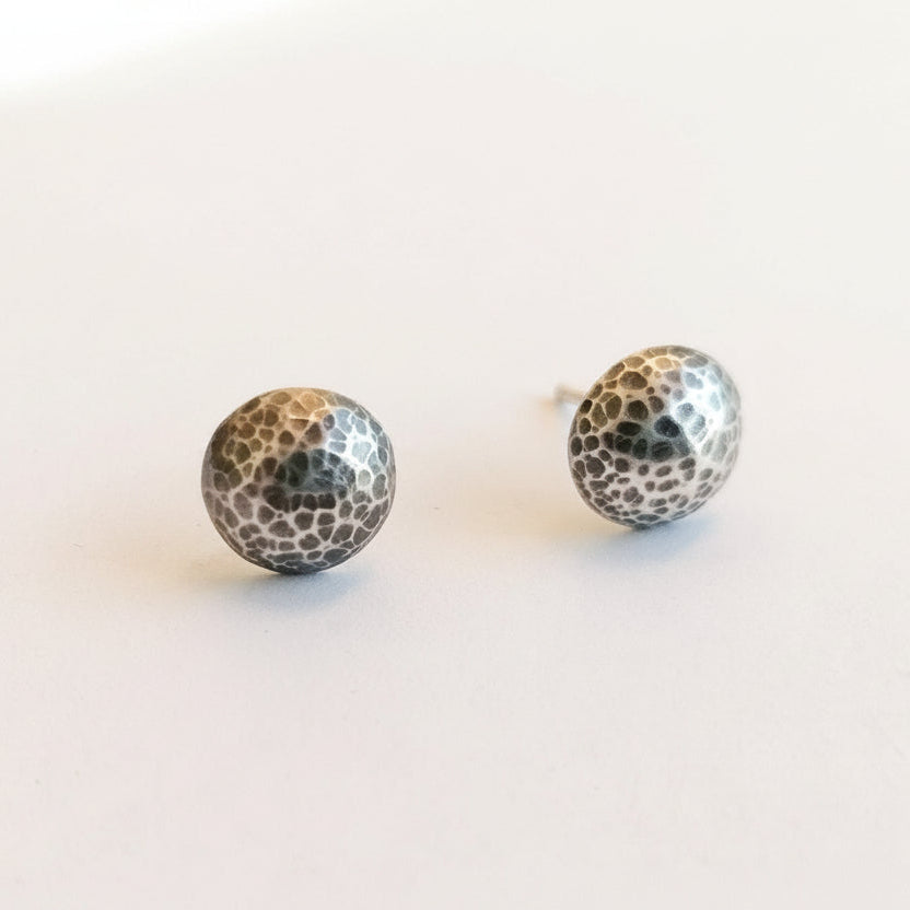 A pair of hammered silver ball stud earrings on a plain white background.