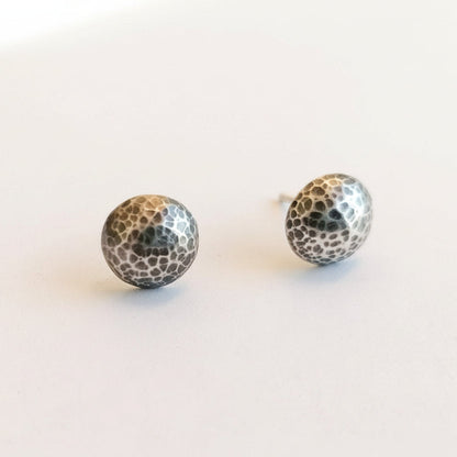 A pair of hammered silver ball stud earrings on a plain white background.
