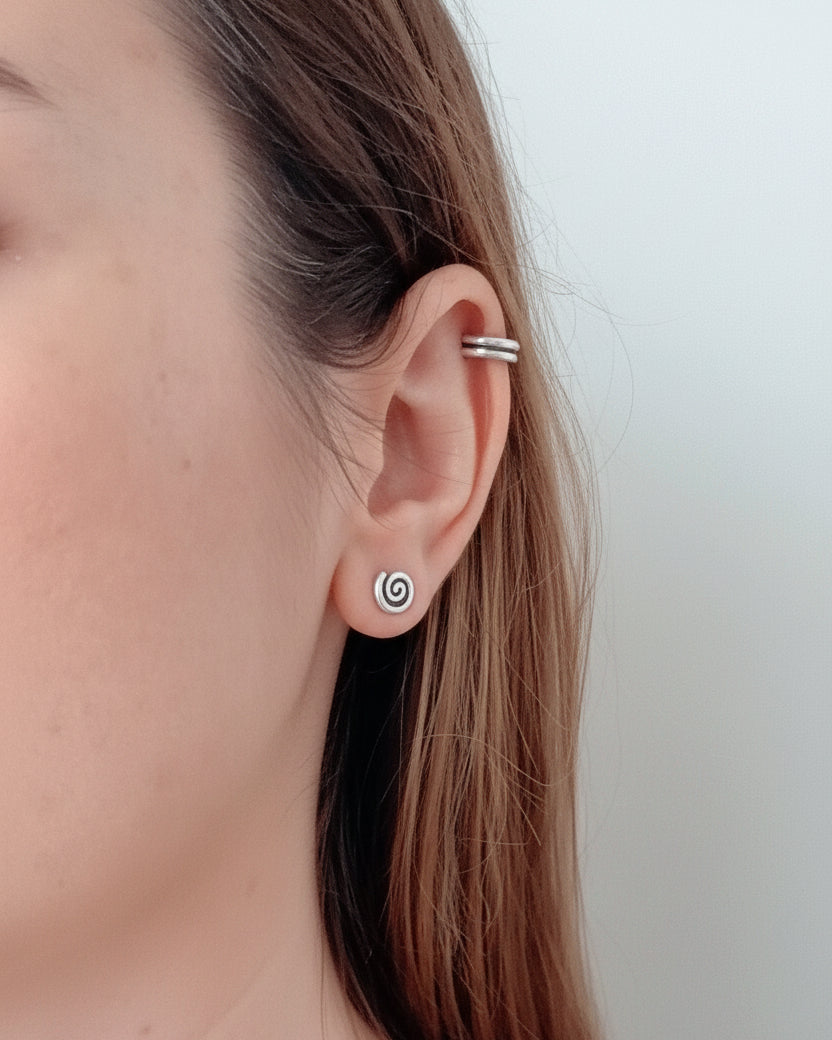 Close-up of an ear with a silver earring on a plain background
