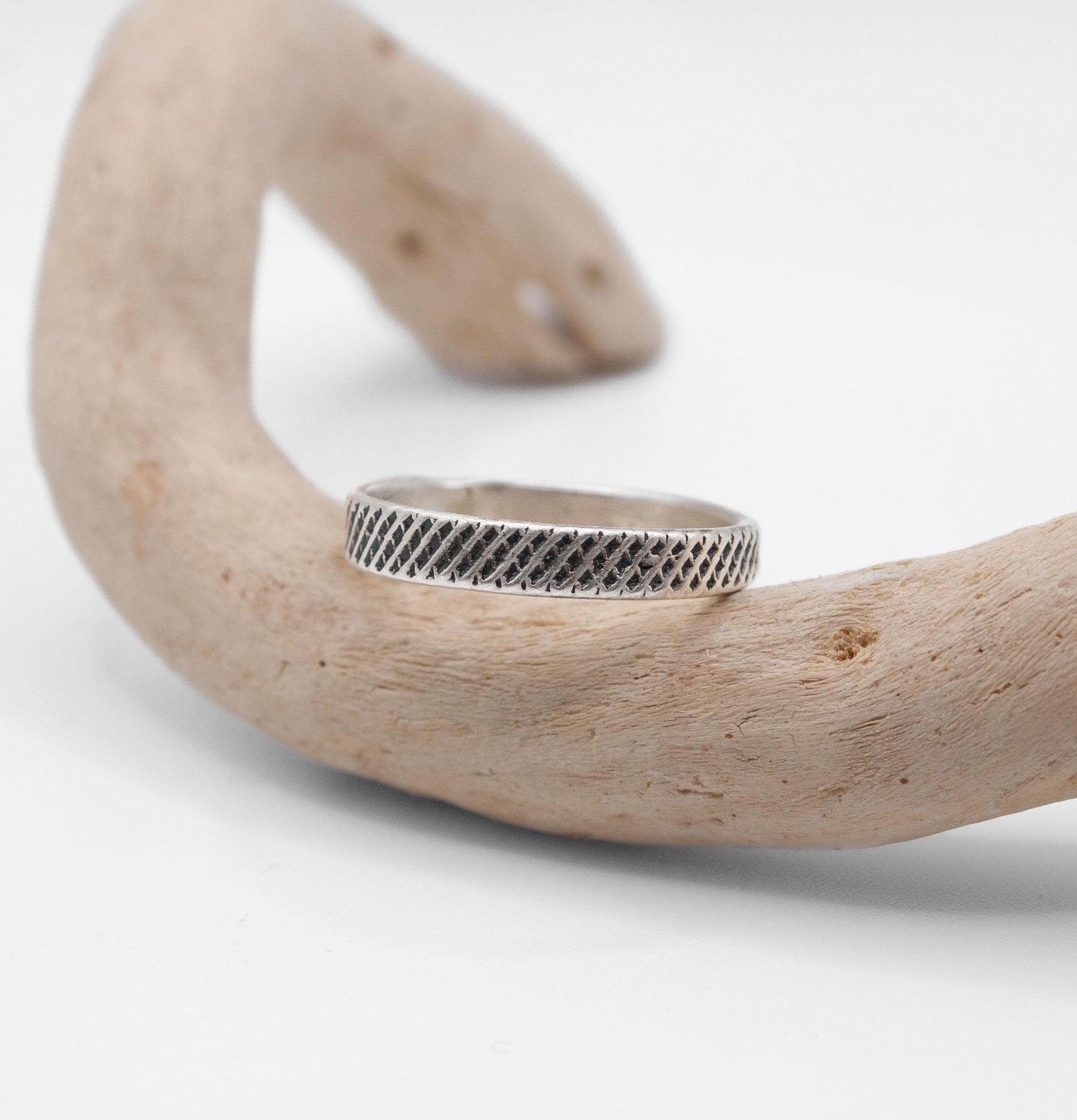 Silver ring with a textured band on a piece of driftwood against a white background