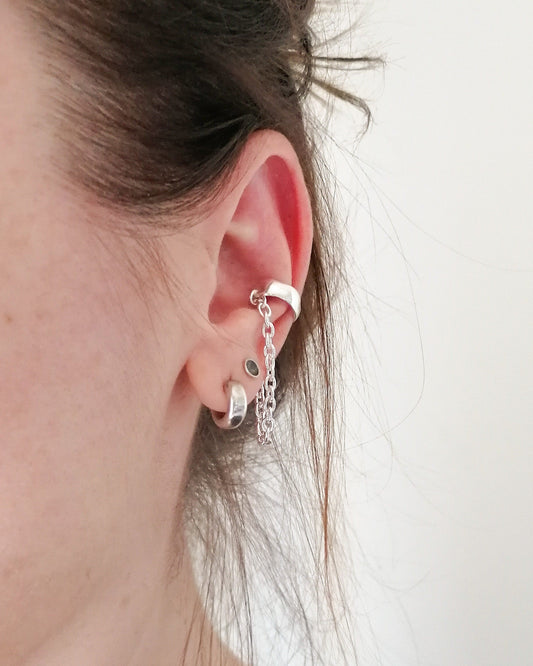 Close-up of an ear wearing a silver earring with a chain detail on a plain background