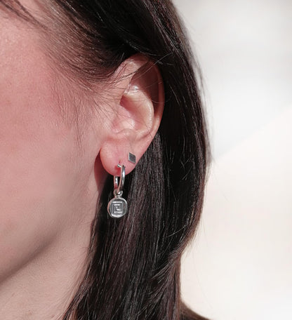 Woman wearing geometric silver hoop and stud earrings, close-up ear jewelry